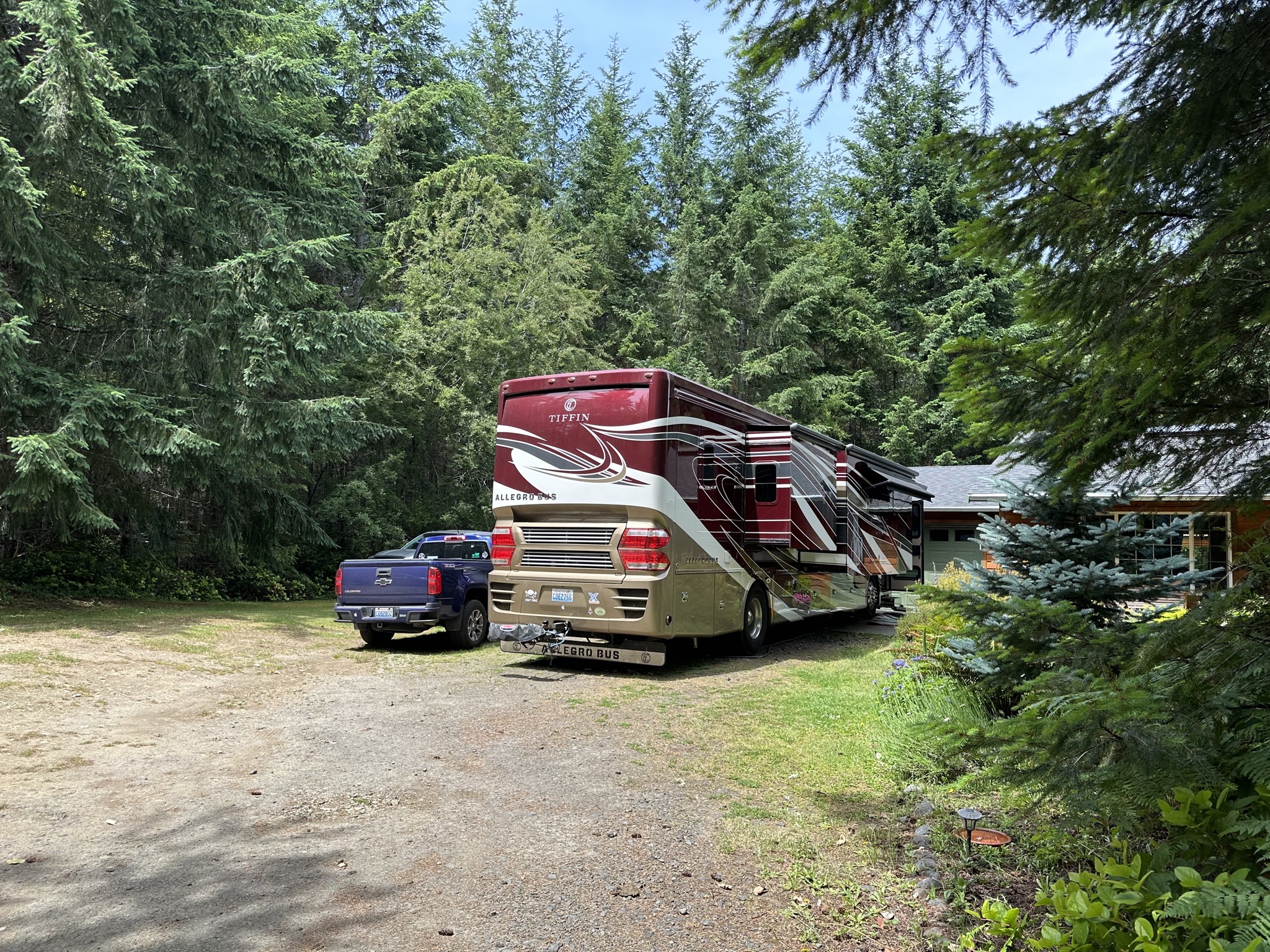 Truck and motorhome parked in front of house, surrounded by trees